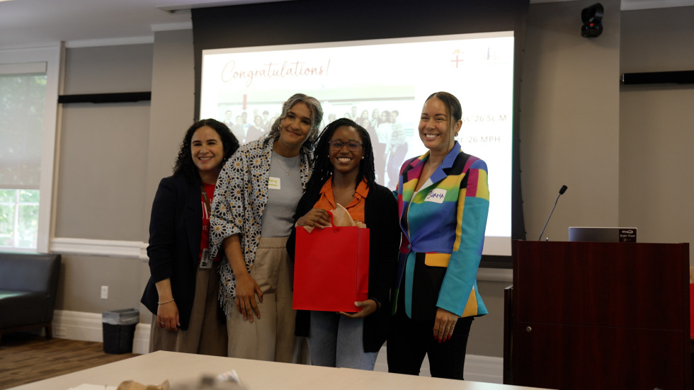 Three university staff members pose with a student holding a red gift bag