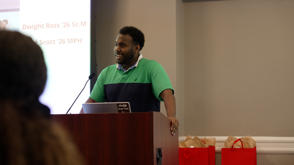 A student is seen sharing remarks in front of a presentation slide and red gift bags.