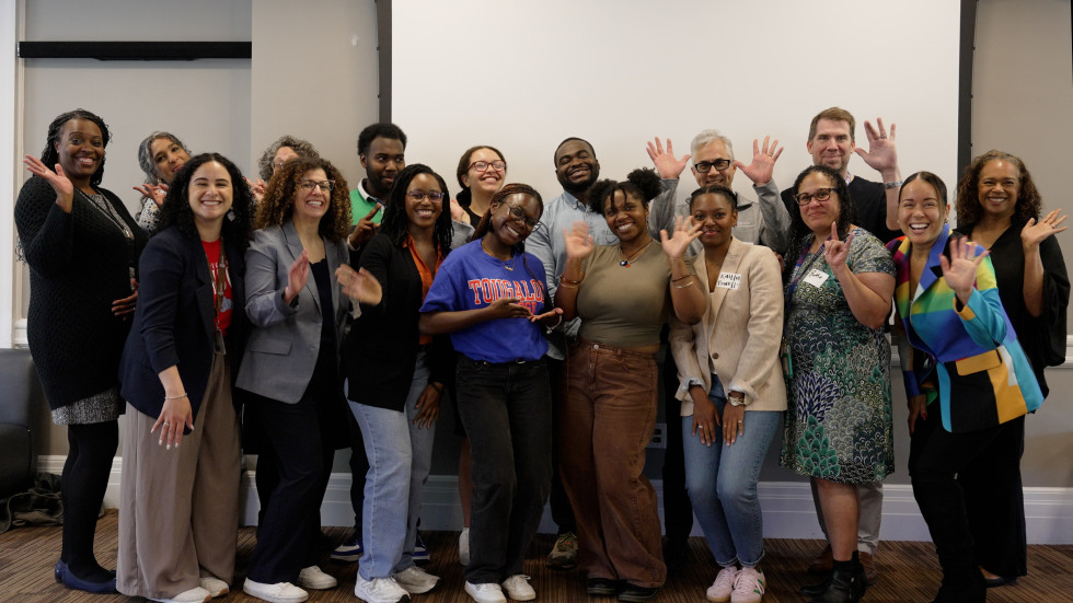 A group of students, faculty, and staff of the Brown-Tougaloo Partnership pose for a photo. They are smiling and waving.
