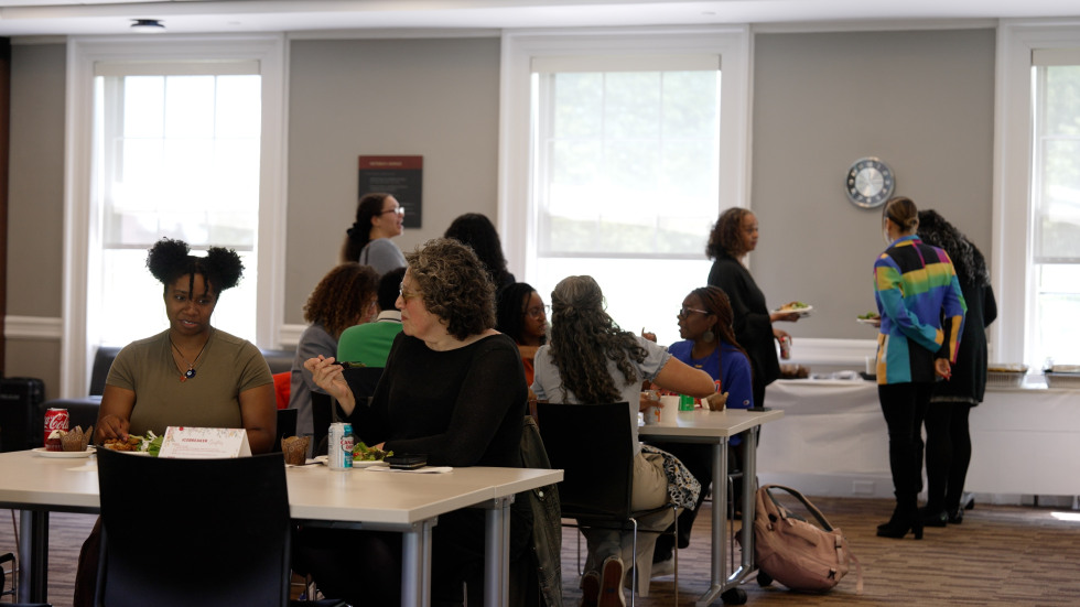 Two people are seen in engaged in conversation as others gather around a food station.