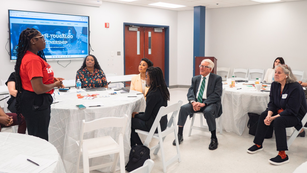 A group of adults who are sitting down listen to a high school student giving a presentation